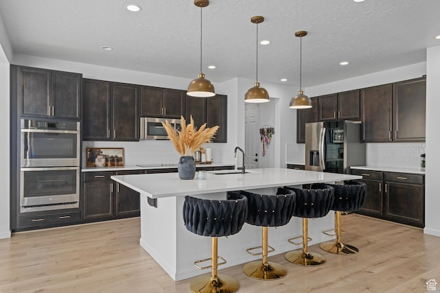 kitchen featuring appliances with stainless steel finishes, pendant lighting, a kitchen breakfast bar, a center island with sink, and light hardwood / wood-style flooring