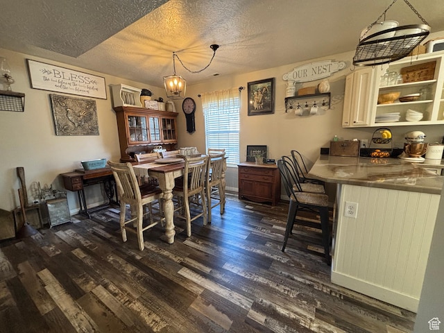 dining area featuring dark wood-style flooring, a textured ceiling, a chandelier, and baseboards