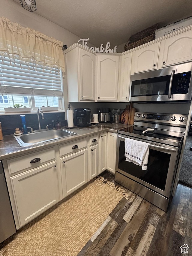 kitchen with stainless steel appliances, a sink, white cabinets, and light wood-style flooring