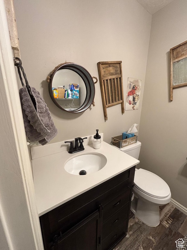 half bath with wood finished floors, toilet, vanity, and baseboards