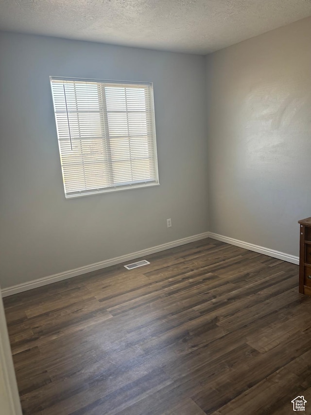 spare room featuring dark wood-style flooring, baseboards, and a textured ceiling