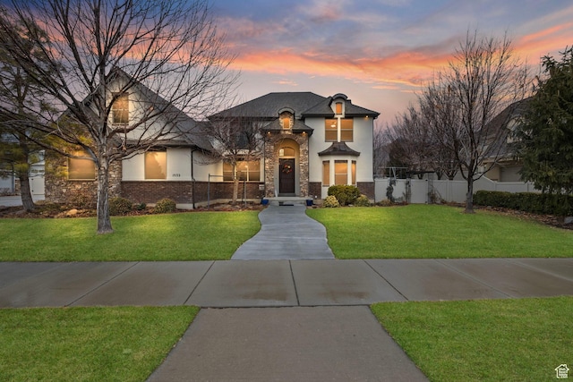 french country style house with stone siding, a yard, stucco siding, and fence
