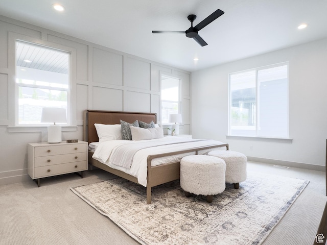 carpeted bedroom featuring recessed lighting, baseboards, a decorative wall, and multiple windows