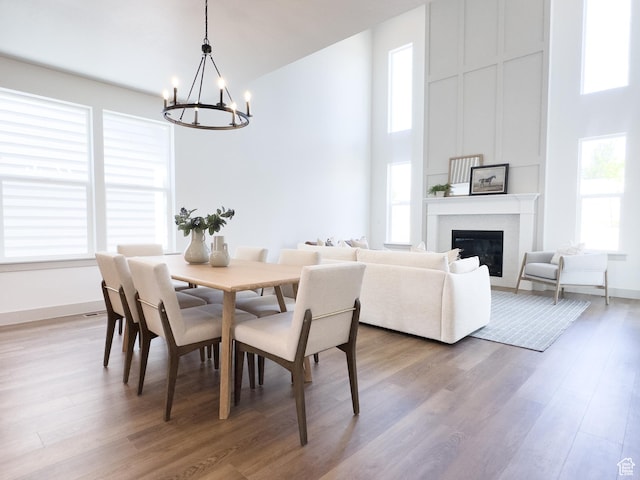 dining area featuring a high ceiling, an inviting chandelier, a glass covered fireplace, and wood finished floors