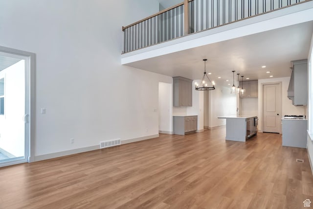 unfurnished living room with a notable chandelier, visible vents, a high ceiling, and light wood-style floors