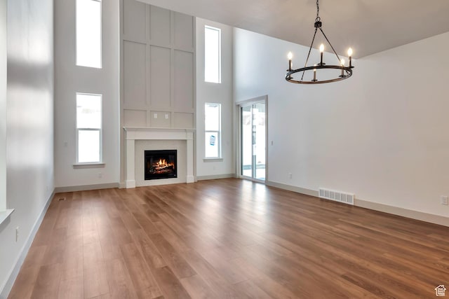 unfurnished living room with visible vents, a glass covered fireplace, a high ceiling, light wood-type flooring, and a notable chandelier