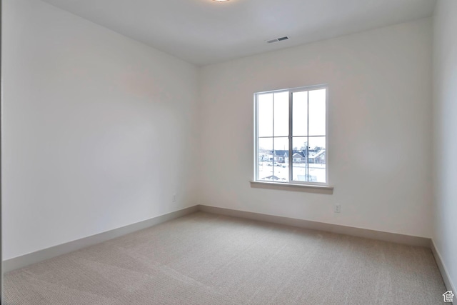 spare room with baseboards, light colored carpet, and visible vents