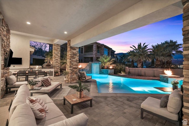 pool at dusk featuring a patio, an outdoor living space with a fireplace, area for grilling, and pool water feature