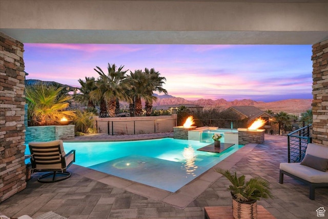 pool at dusk with pool water feature, a mountain view, a patio area, and a fire pit