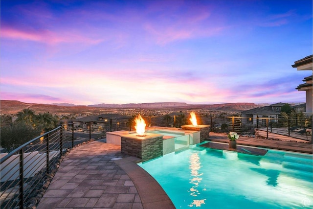 pool at dusk with a patio, a mountain view, and an outdoor fire pit