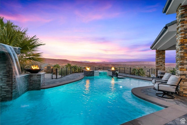 pool at dusk featuring pool water feature, a mountain view, and a patio area