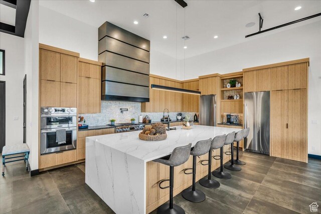kitchen with a breakfast bar, a center island with sink, stainless steel appliances, light stone countertops, and a high ceiling