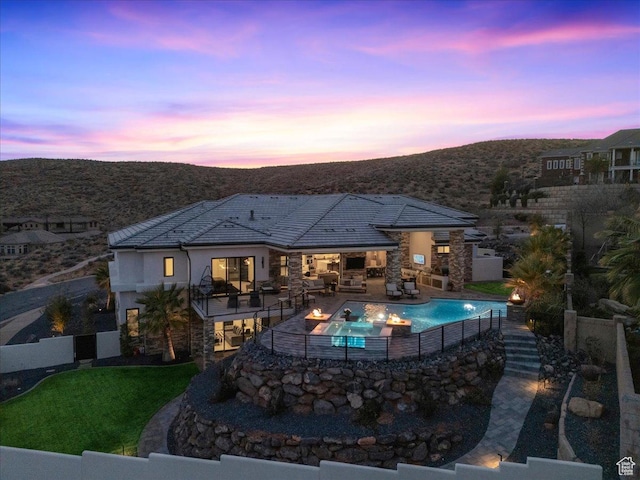 pool at dusk featuring a mountain view, a fireplace, a lawn, and a patio area