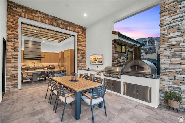 patio terrace at dusk featuring a grill, sink, and exterior kitchen