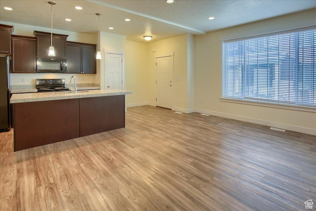 kitchen with dark brown cabinets, hanging light fixtures, a kitchen island with sink, light hardwood / wood-style floors, and black appliances