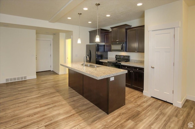 kitchen with hanging light fixtures, dark brown cabinets, black appliances, a center island with sink, and light wood-type flooring