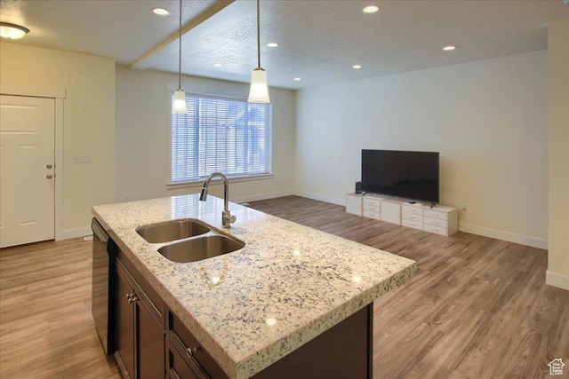 kitchen with sink, hanging light fixtures, black dishwasher, an island with sink, and light wood-type flooring