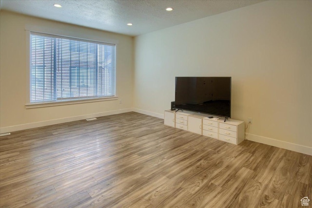 unfurnished living room with light hardwood / wood-style flooring and a textured ceiling