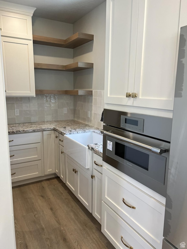 kitchen with white cabinetry, stainless steel appliances, dark hardwood / wood-style floors, light stone counters, and decorative backsplash