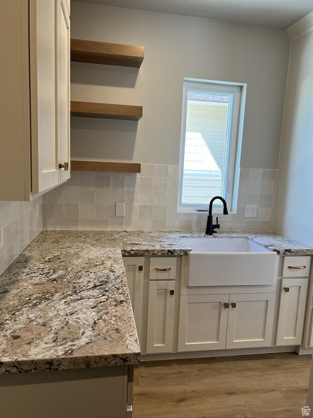 kitchen with white cabinetry, sink, backsplash, light stone counters, and light hardwood / wood-style floors