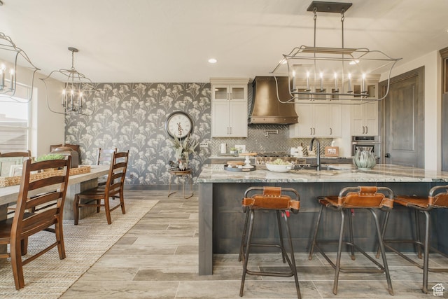 kitchen featuring pendant lighting, wall chimney range hood, light stone countertops, and a chandelier