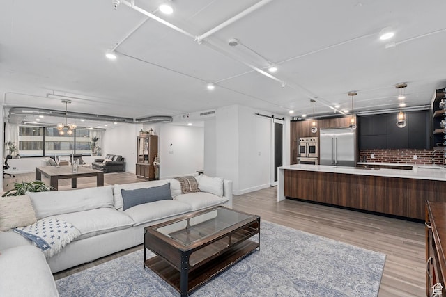 living room with sink, a notable chandelier, a barn door, and light wood-type flooring