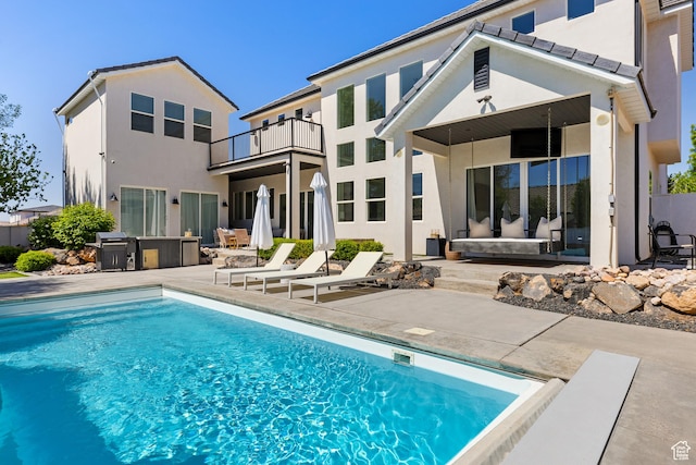 rear view of house featuring a fenced in pool, a patio area, stucco siding, and a balcony