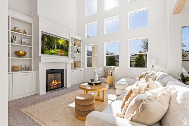 living area with carpet, a towering ceiling, a glass covered fireplace, and built in shelves