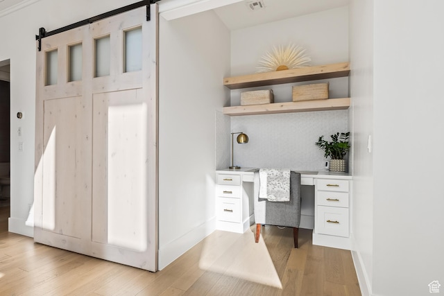 office with built in study area, a barn door, and light wood-style floors