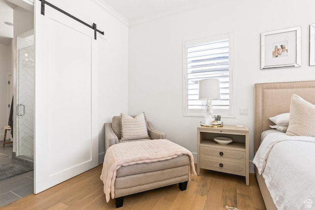 bedroom with a barn door, light wood-style floors, and ornamental molding