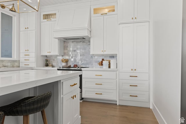 kitchen with white cabinets, custom exhaust hood, light wood-type flooring, and backsplash