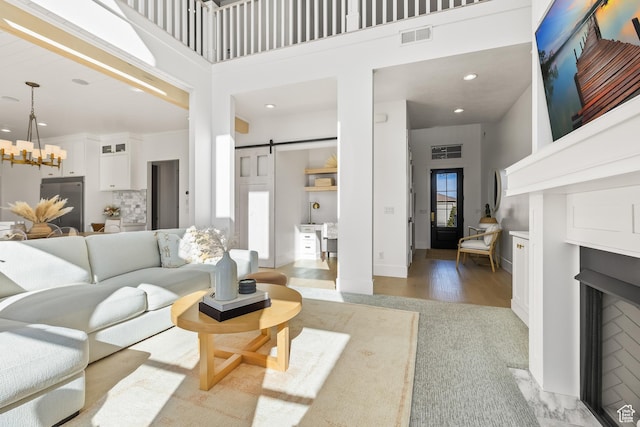 living room featuring a chandelier, a high ceiling, a fireplace with flush hearth, a barn door, and visible vents