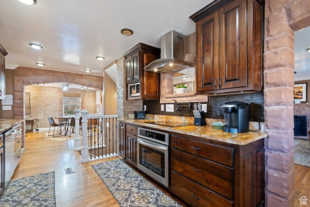 75 N 200 W, Kanab, UT 84741 - kitchen featuring dark brown cabinets, appliances with stainless steel finishes, light stone countertops, light hardwood / wood-style floors, and wall chimney range hood