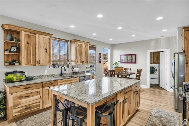kitchen with light stone counters, stainless steel appliances, washer / clothes dryer, and sink
