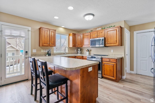 700 S Clearwater Falls Dr E, Layton, UT 84041 - kitchen featuring sink, appliances with stainless steel finishes, a kitchen breakfast bar, a textured ceiling, and light wood-type flooring