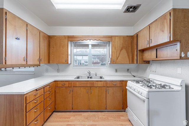 kitchen with sink, backsplash, white gas stove, and light wood-type flooring