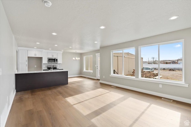unfurnished living room featuring visible vents, baseboards, recessed lighting, an inviting chandelier, and wood finished floors