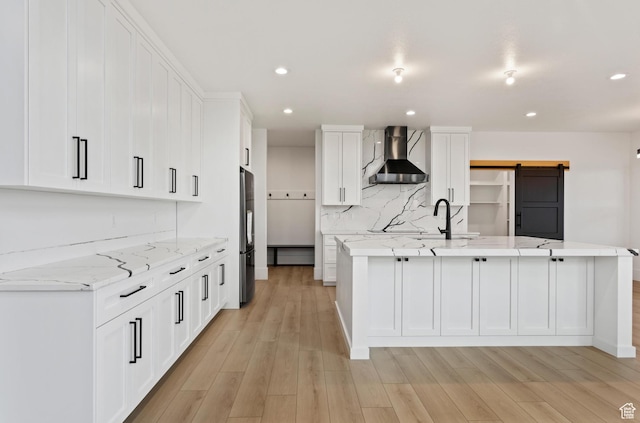 124 E 4100 N, North Ogden, UT 84414 - kitchen featuring wall chimney range hood, stainless steel refrigerator, white cabinetry, light stone countertops, and a barn door
