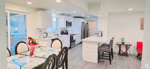1600 W 4300 S, Salt Lake City, UT 84123 - kitchen featuring stainless steel appliances, a sink, light wood-style floors, a kitchen breakfast bar, and white cabinets