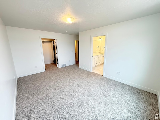 unfurnished bedroom featuring baseboards, visible vents, light colored carpet, a walk in closet, and a textured ceiling