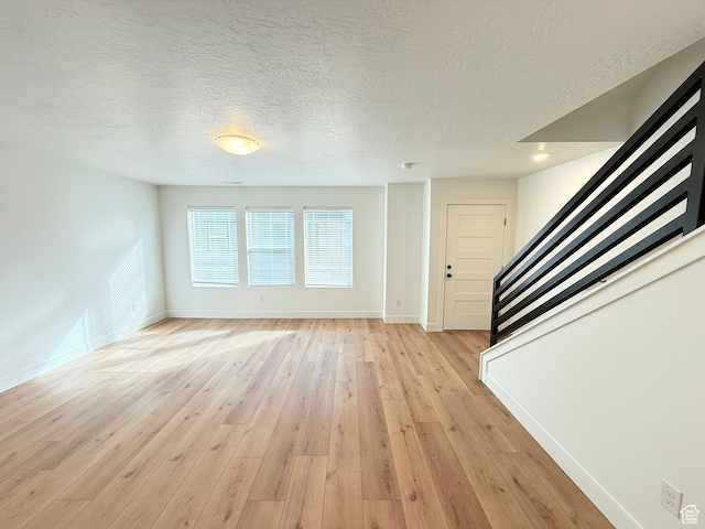 unfurnished living room featuring light wood-type flooring, a textured ceiling, baseboards, and stairs