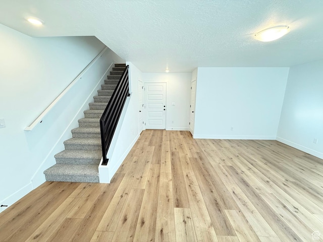 stairs featuring a textured ceiling, baseboards, and wood finished floors