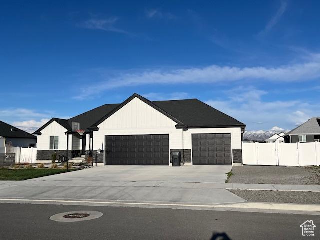 modern farmhouse with stone siding, fence, a gate, an attached garage, and driveway