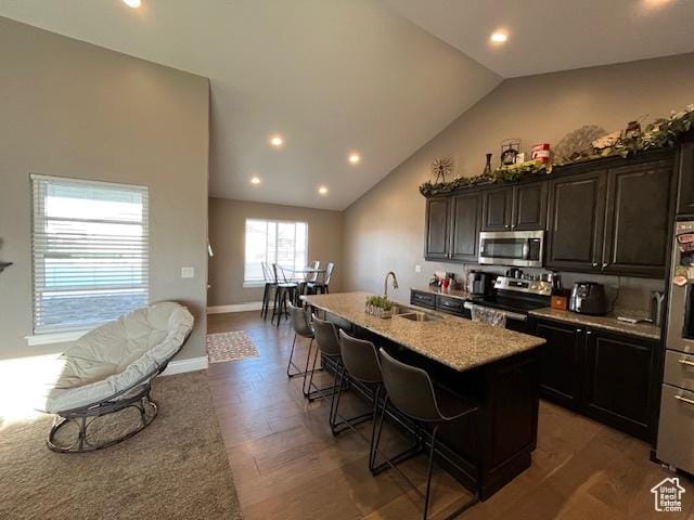 kitchen with baseboards, a center island with sink, a kitchen bar, stainless steel appliances, and a sink
