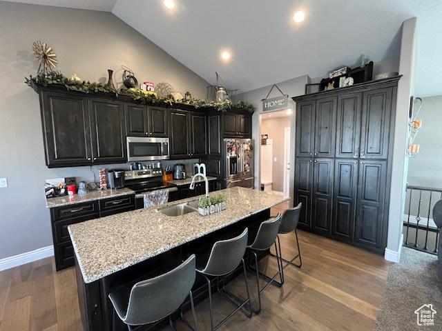 kitchen with an island with sink, light wood-type flooring, a sink, stainless steel appliances, and a breakfast bar area