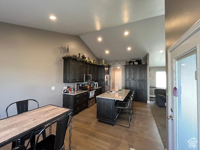 kitchen featuring appliances with stainless steel finishes, a breakfast bar, an island with sink, lofted ceiling, and a sink