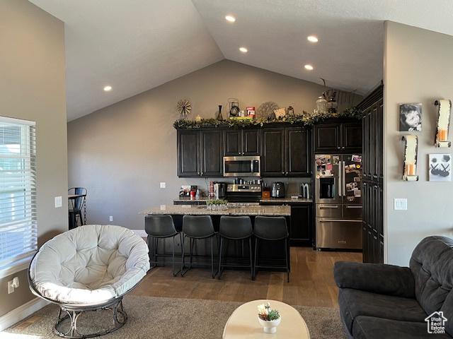 kitchen with appliances with stainless steel finishes, wood finished floors, lofted ceiling, open floor plan, and a breakfast bar area