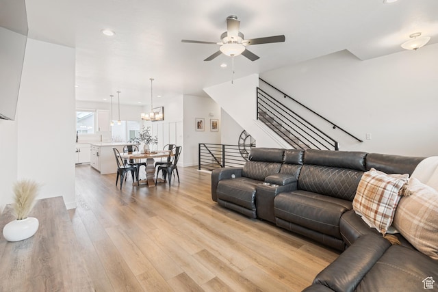 living room with ceiling fan with notable chandelier and light hardwood / wood-style flooring