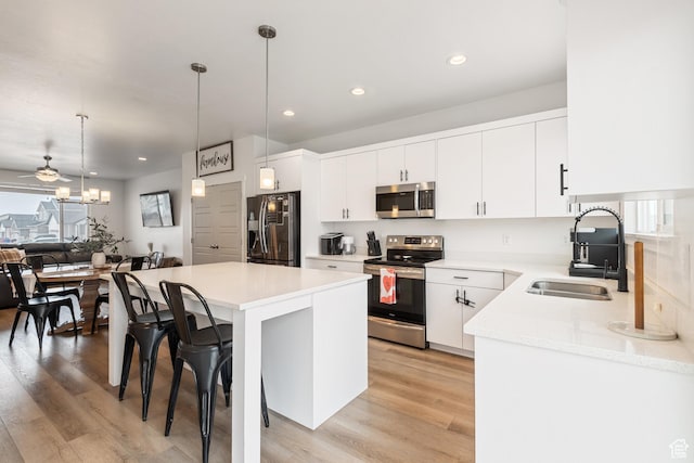 kitchen with sink, decorative light fixtures, a kitchen island, stainless steel appliances, and white cabinets