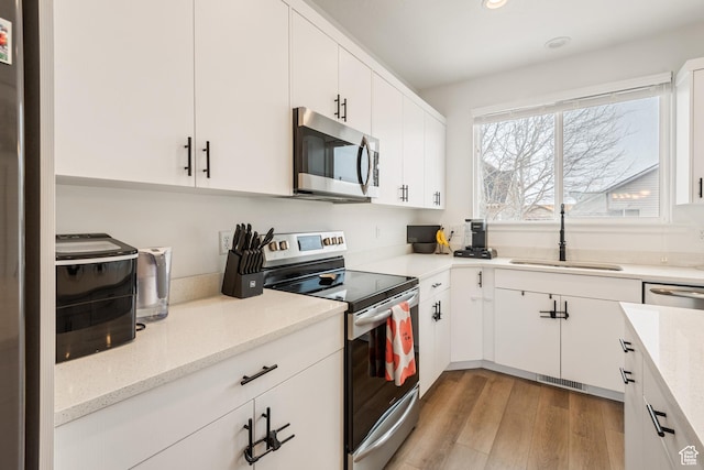 kitchen with appliances with stainless steel finishes, light hardwood / wood-style floors, sink, and white cabinets